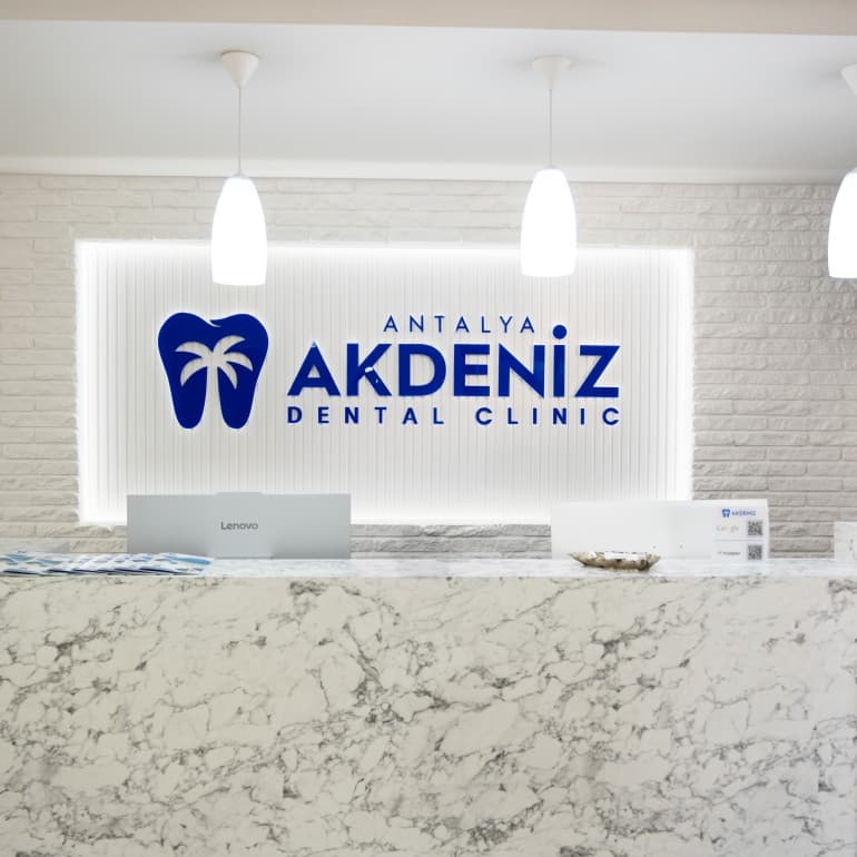 Recepcja kliniki Akdeniz Dental w Antalyi z podświetlonym logo i marmurową ladą