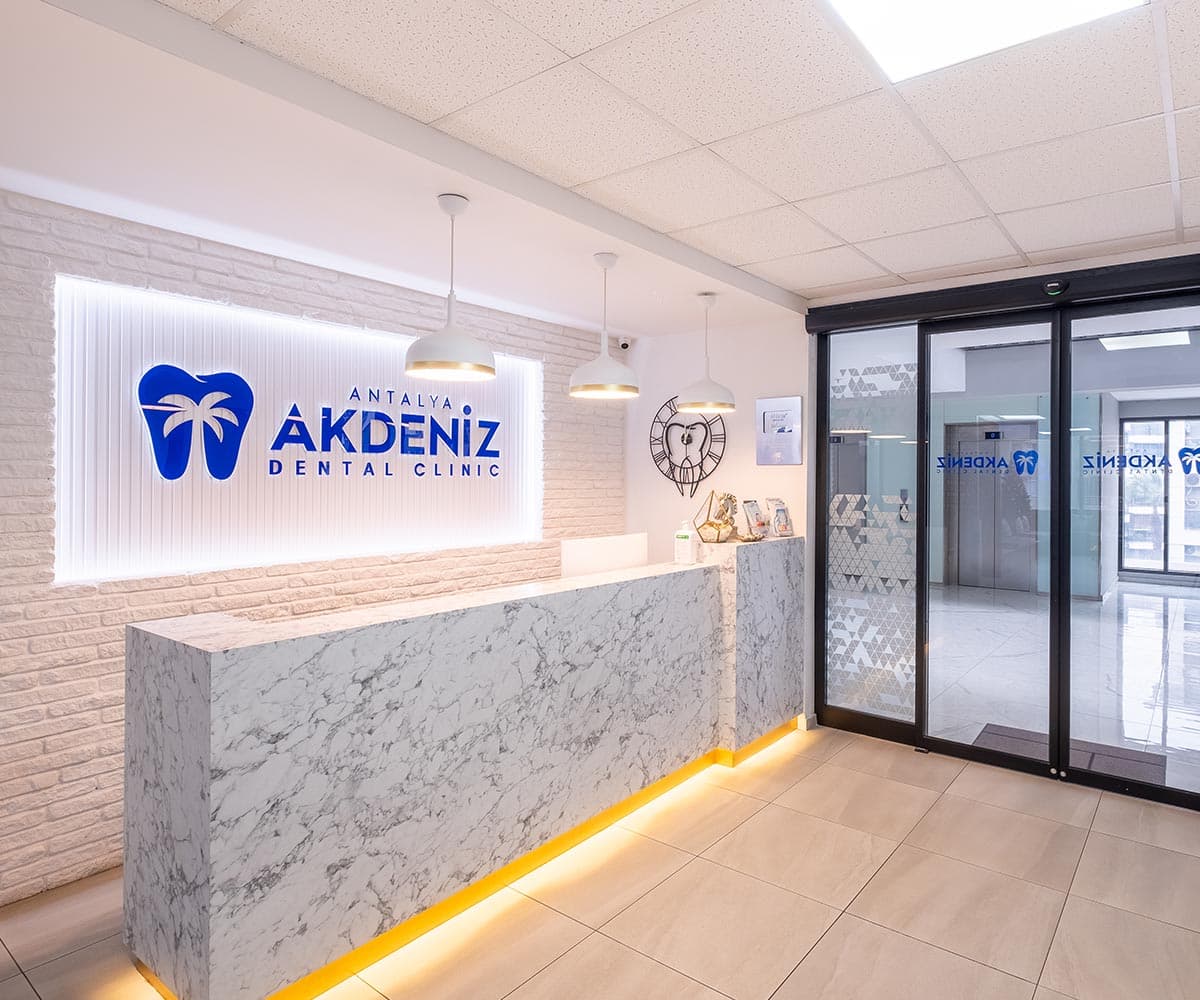 Recepcja i wejście do kliniki Akdeniz Dental: podświetlone logo na ceglanej ścianie i marmurowa lada